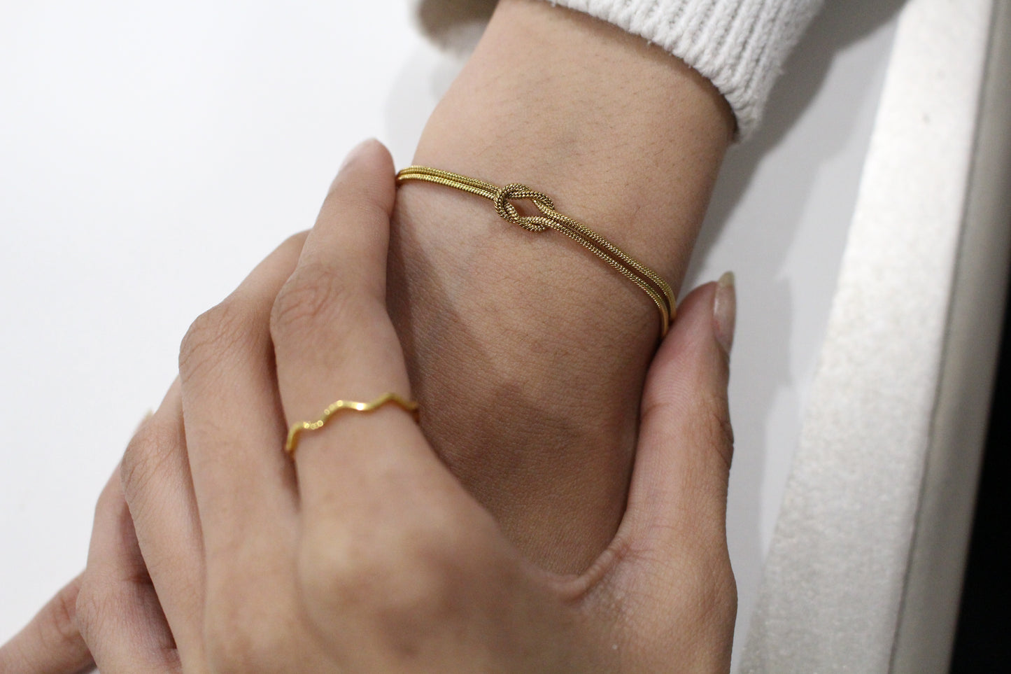 Close-up of a hand wearing two gold bracelets on a white background