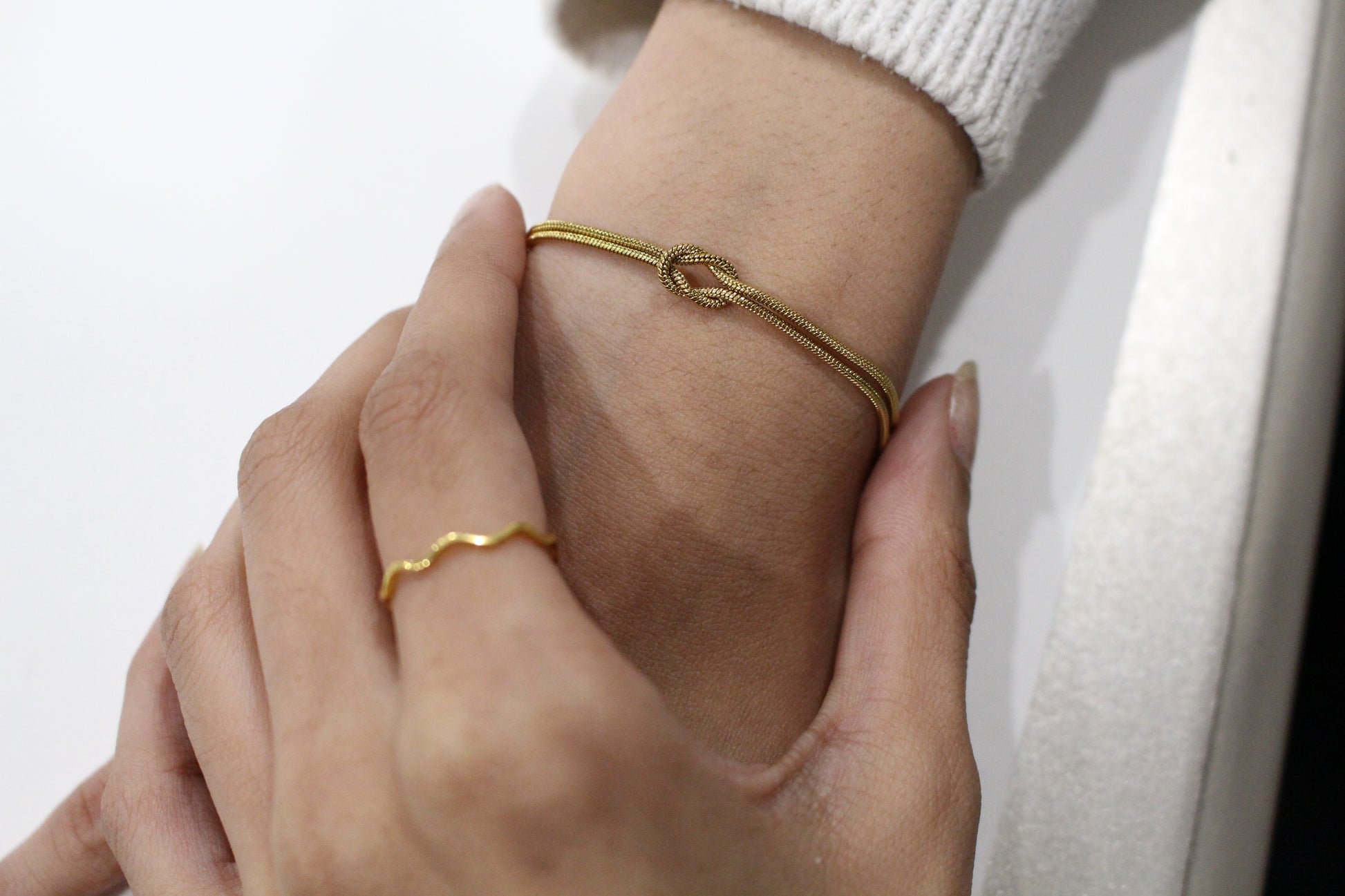 Close-up of a hand wearing two gold bracelets on a white background