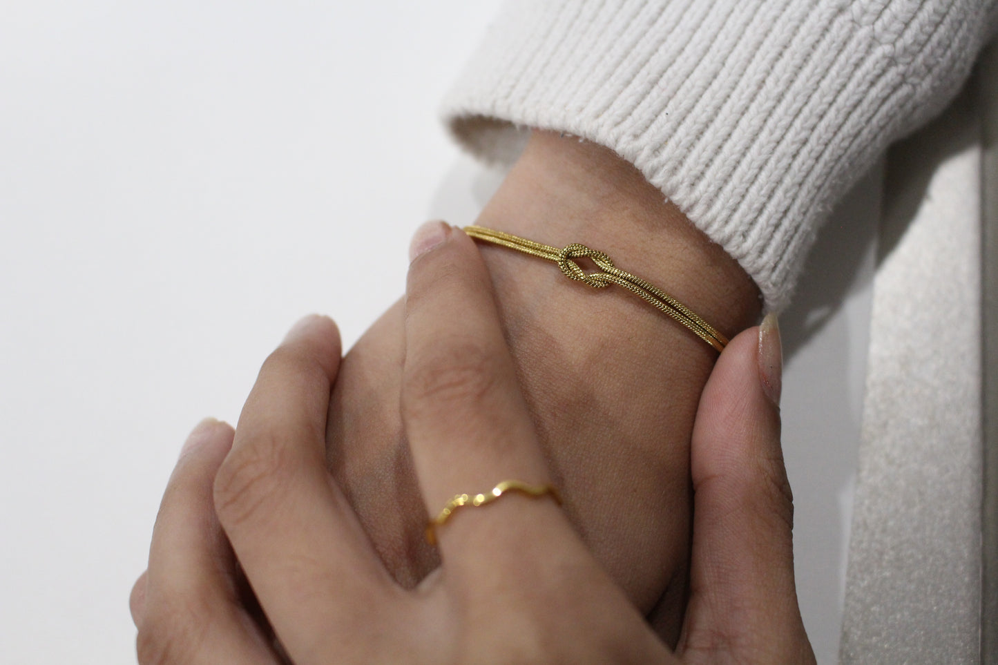 Close-up of hands wearing gold bracelets on a plain background