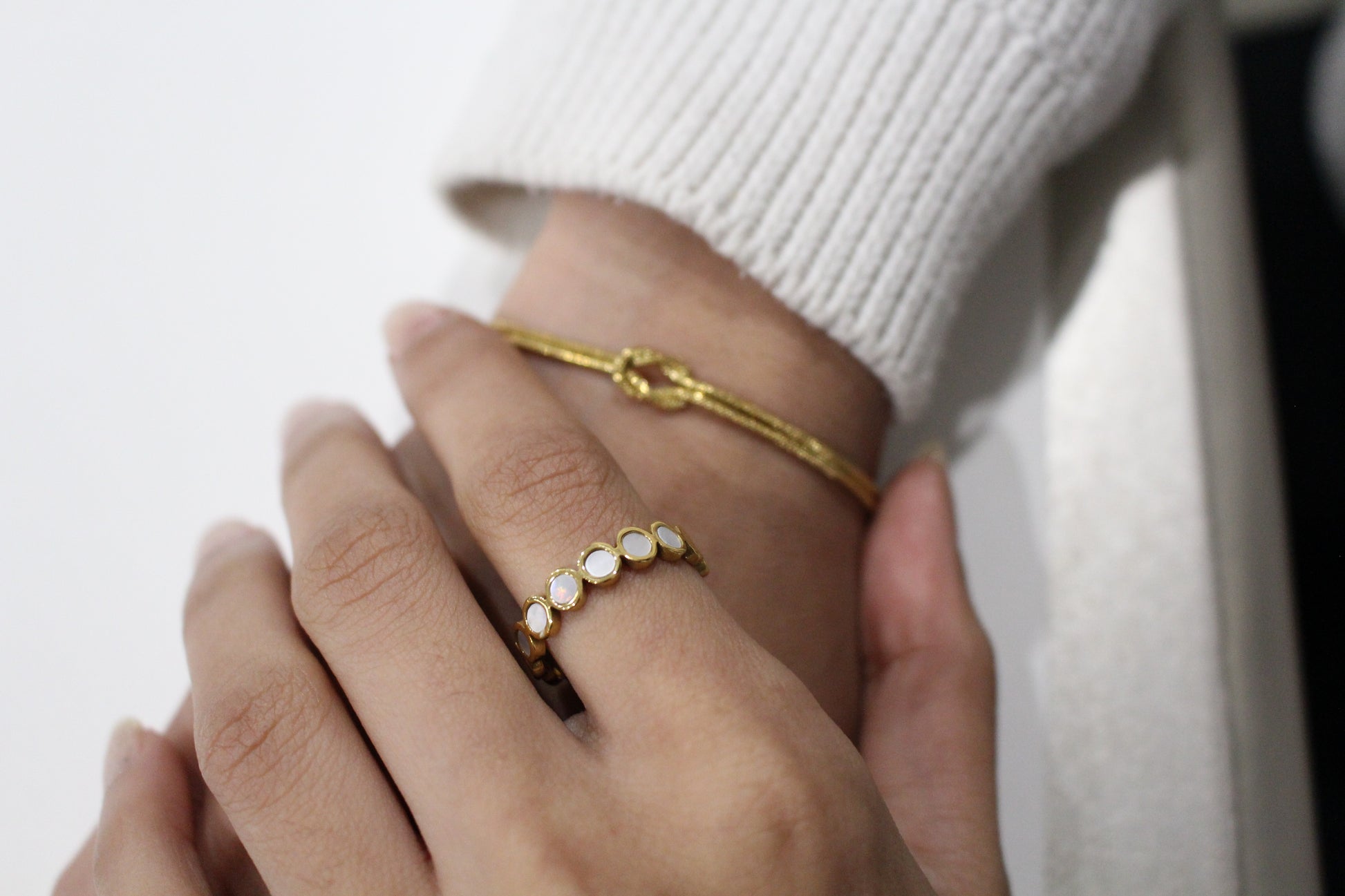 Close-up of a hand wearing a gold ring with small stones on a plain background