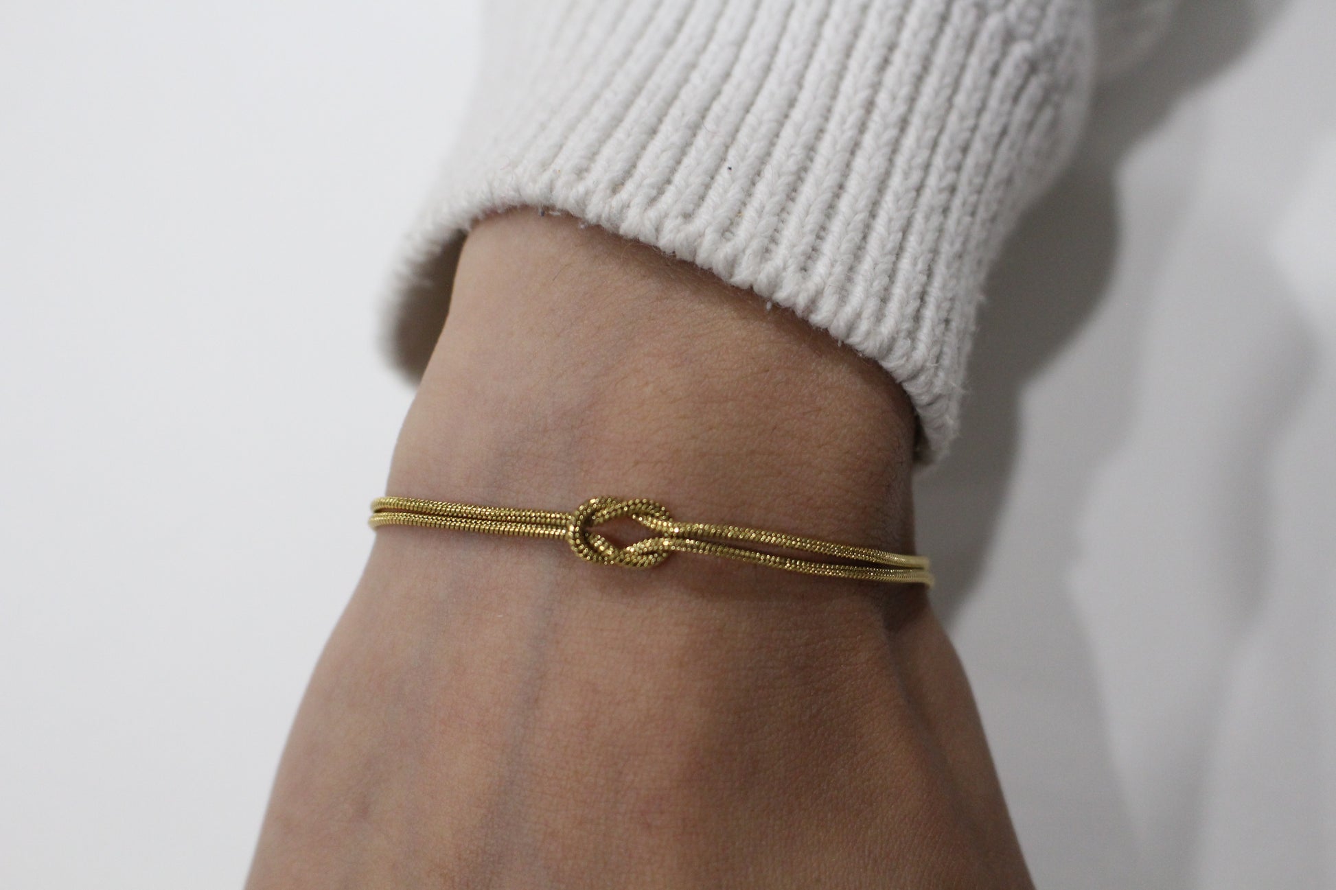 Gold bracelet on a wrist with a plain background