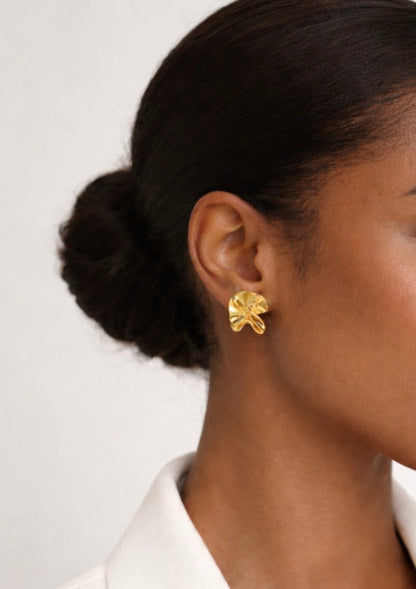 Gold floral earring worn by a person with a neutral background