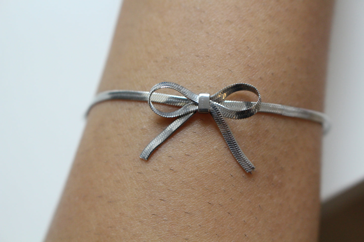Silver bow-shaped bracelet on a wrist against a neutral background
