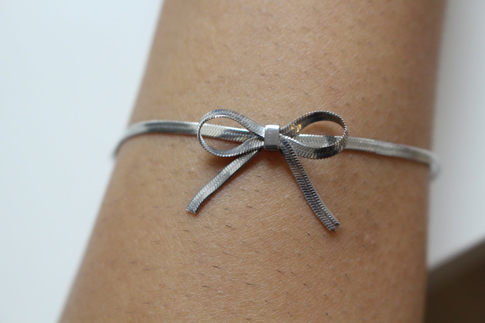 Silver bow-shaped bracelet on a wrist against a neutral background
