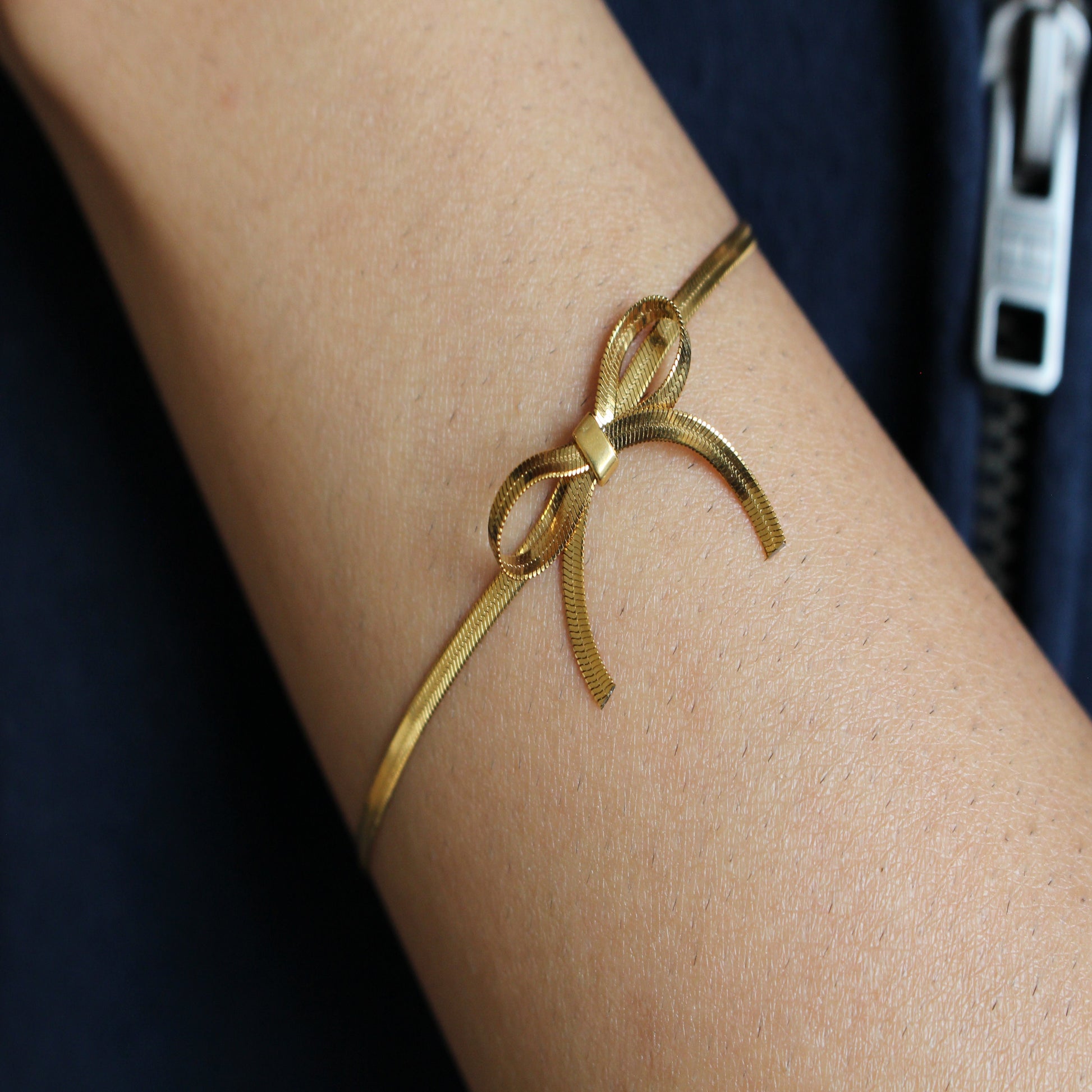 Gold bow-shaped bracelet on a wrist with a blurred background